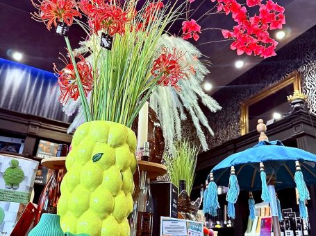 
„Dekobereich im BSix® Conceptstore mit großer gelber Ananasvase, Kunstblumenarrangement und farbigen Wohnaccessoires.“