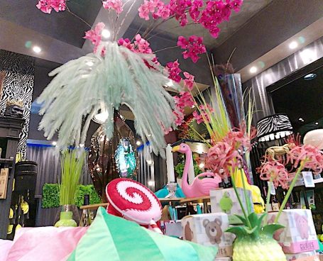 „Deko-Arrangement im BSix® Conceptstore mit großem weißen Federbouquet, pinken Blüten und Geschenkartikeln auf einem Tisch.“