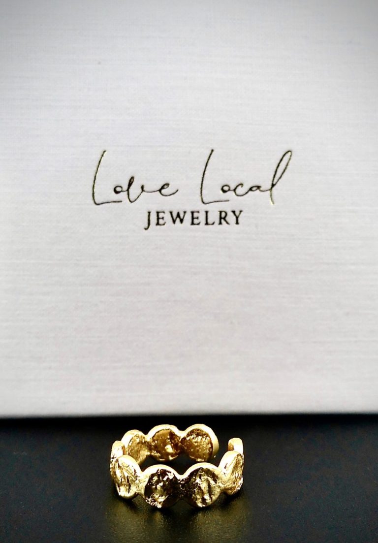 Schmuckring vor neutralem Hintergrund mit Markenaufdruck „Love Local Jewelry“
