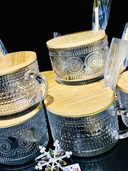 Mehrere dekorative Glasbehälter mit geprägtem Muster und Holzdeckeln, arrangiert auf einer dunklen Fläche.