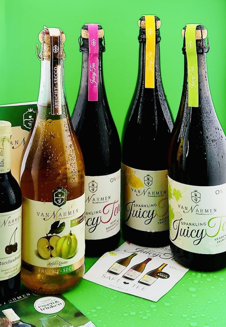 Mehrere Flaschen alkoholfreier Fruchtsekt-Getränke verschiedener Sorten in Glasflaschen vor grünem Hintergrund